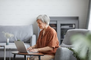 Seitenansichtsporträt einer älteren Geschäftsfrau, die einen Laptop benutzt, während sie von zu Hause aus arbeitet, in minimalem Innenraum, Kopierraum
