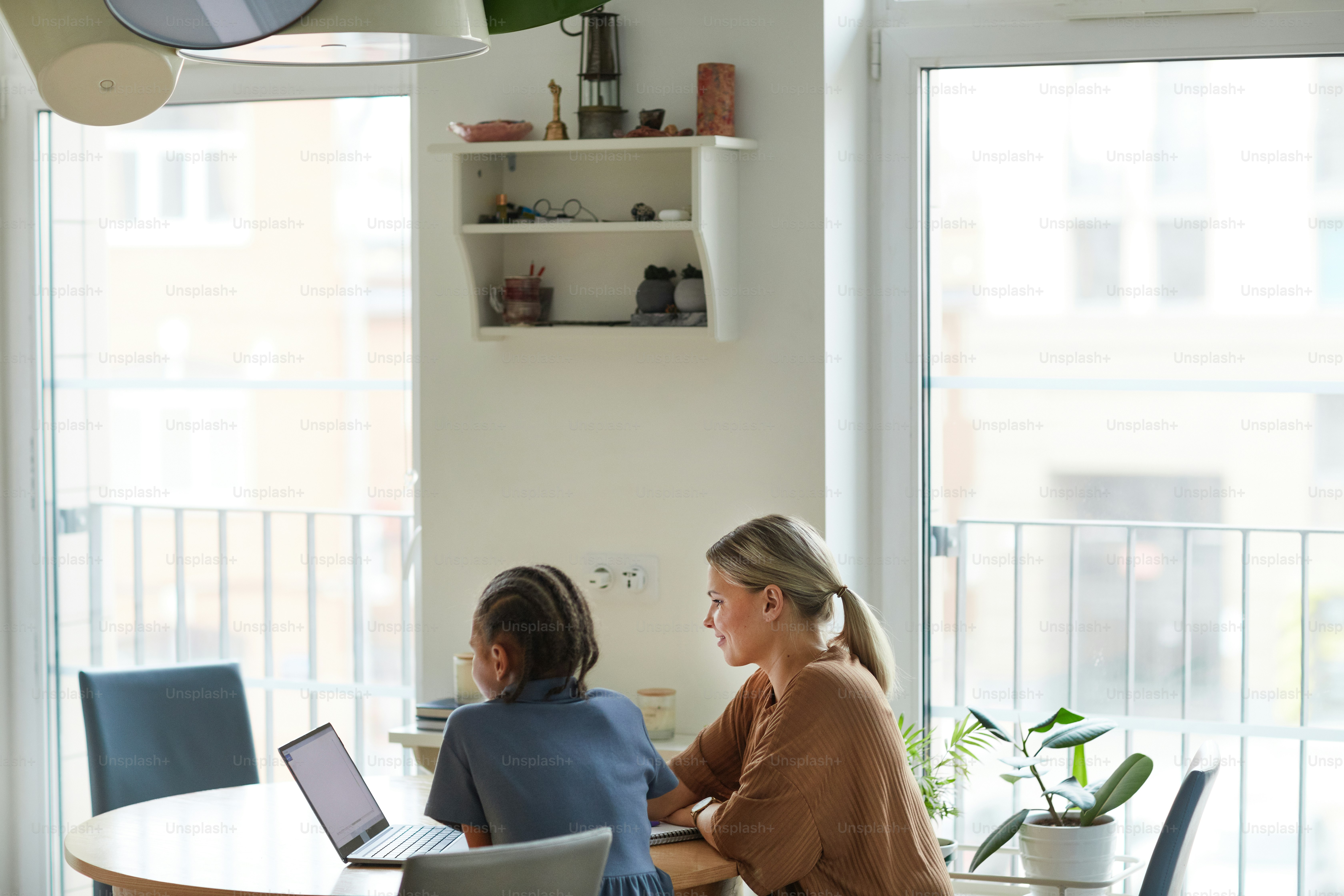 Minimal shot of multiethnic family, mother and daughter looking at laptop screen while studying together at home in minimal setting, copy space