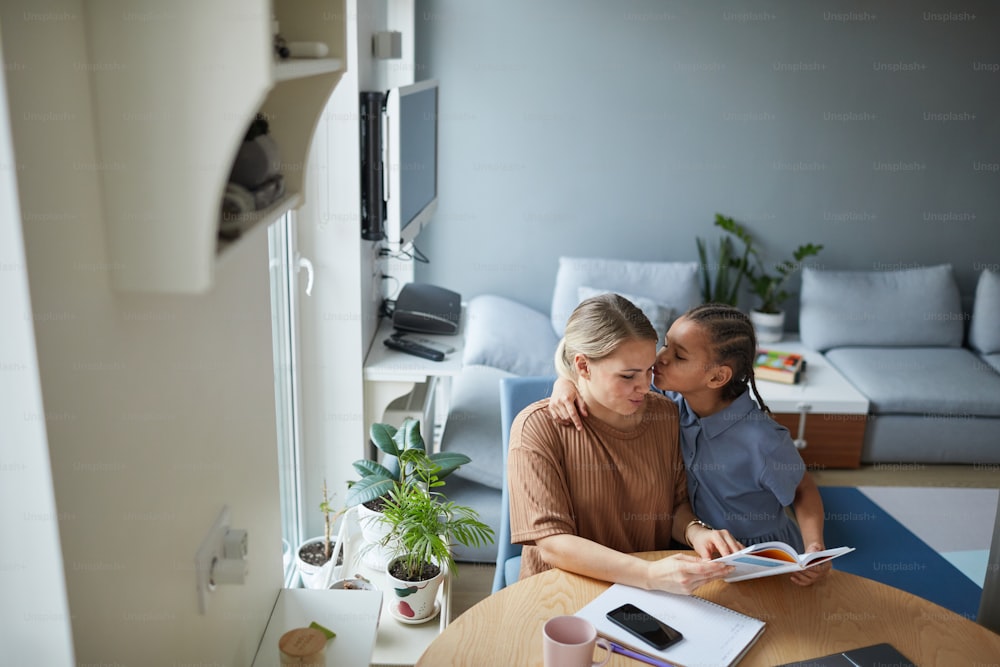 High angle portrait of young black girl kissing Caucasian mother in cute multiethnic family scene, copy space