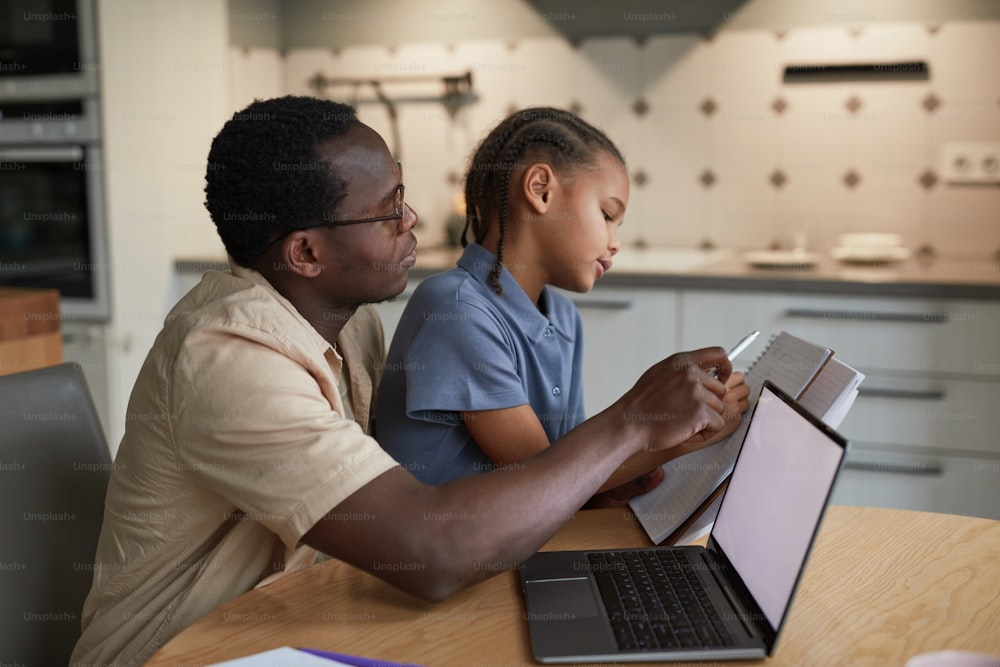 Seitenansichtsporträt des fürsorglichen schwarzen Vaters, der der Tochter bei den Hausaufgaben hilft, in gemütlicher Szene, Kopierraum