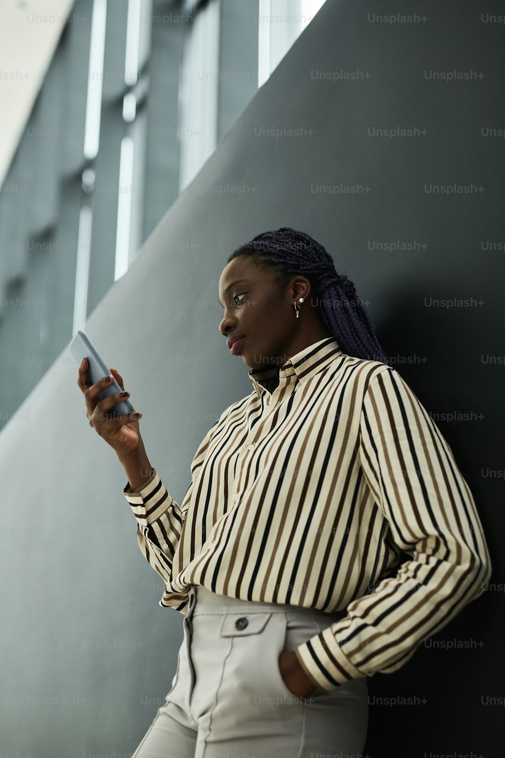 Graphic side view portrait of confident African-American businesswoman holding smartphone while standing against black background