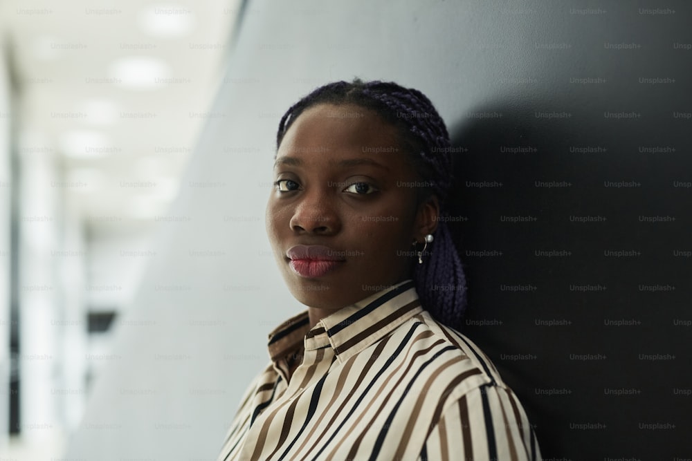 Close up portrait of young African-American businesswoman looking at camera while standing against black background in office
