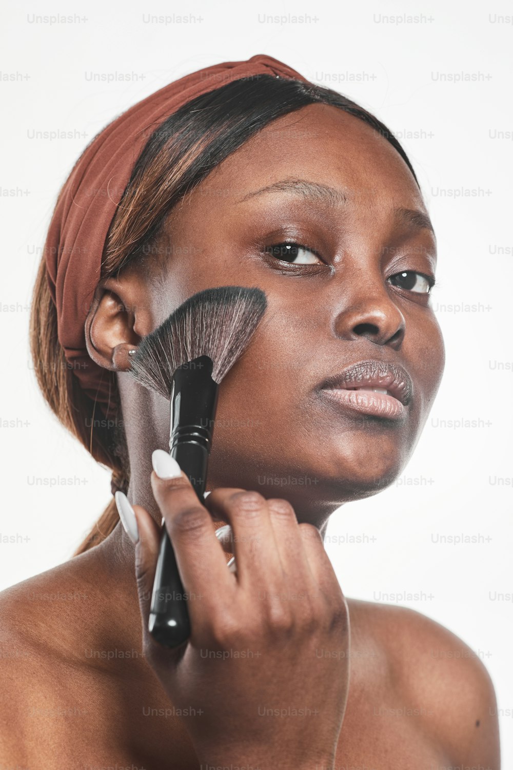 Vertical portrait of young African-American woman applying makeup against white background, isolated cut out