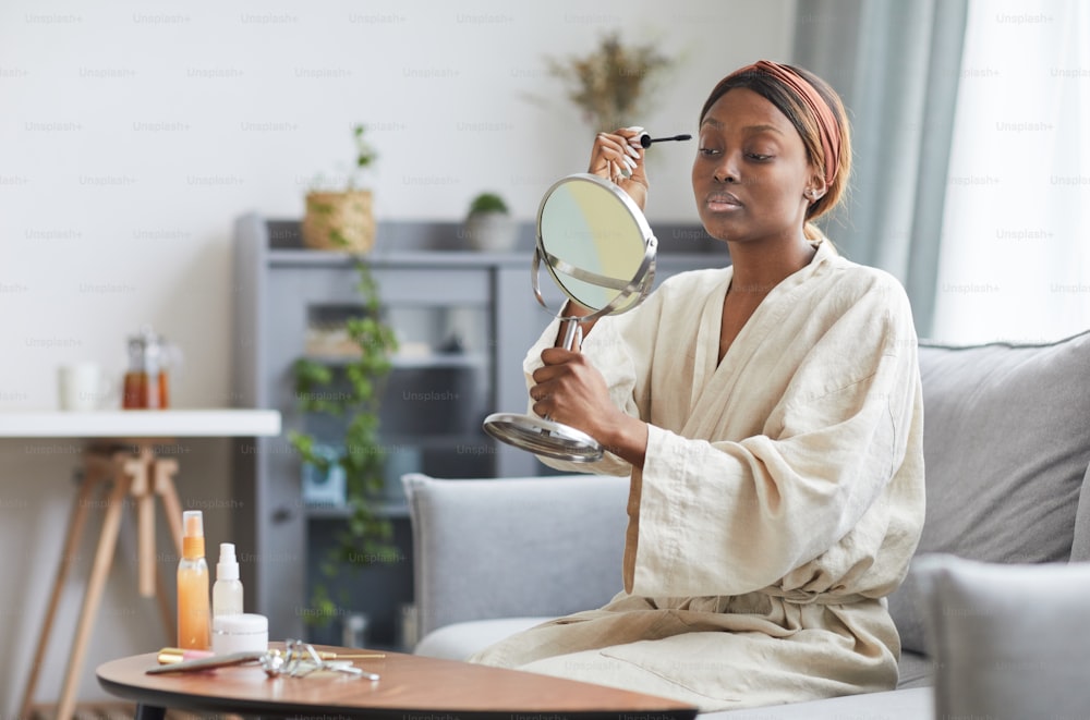 Portrait of young African-American woman doing makeup at home in morning, copy space