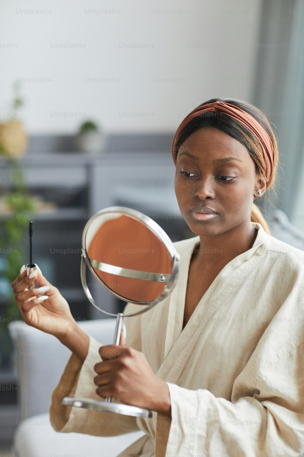 Vertical portrait of young African-American woman doing makeup at home in morning