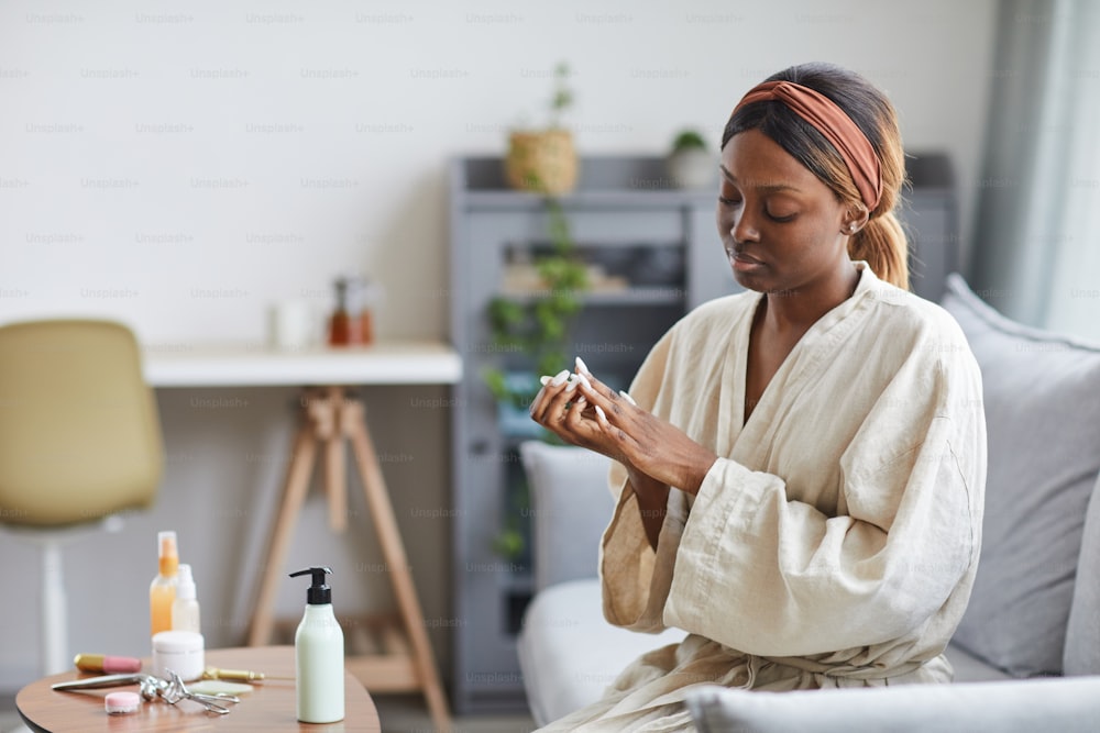 Portrait d’une jeune femme afro-américaine utilisant une crème pour les mains ou une crème hydratante, concept de routine de soin et de beauté, espace de copie