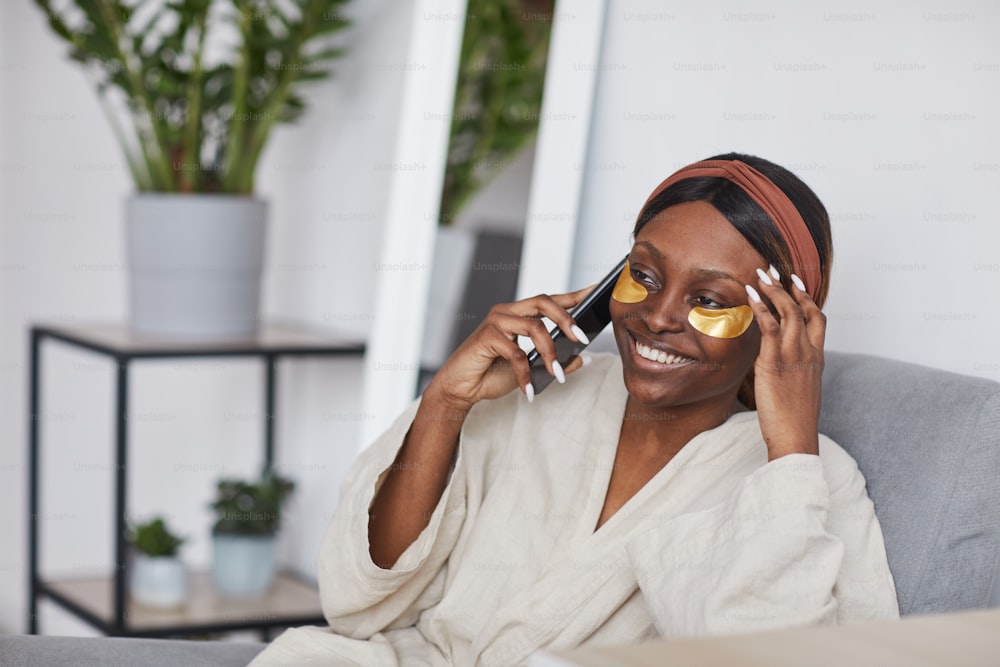 Portrait minimal d’une belle femme afro-américaine parlant par smartphone tout en profitant de la routine de soins de la peau à la maison, espace de copie