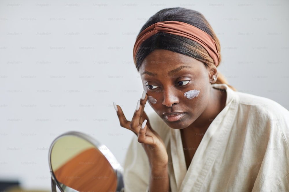 Minimal portrait of young African-American woman using face cream or moisturizer, skincare and beauty routine concept