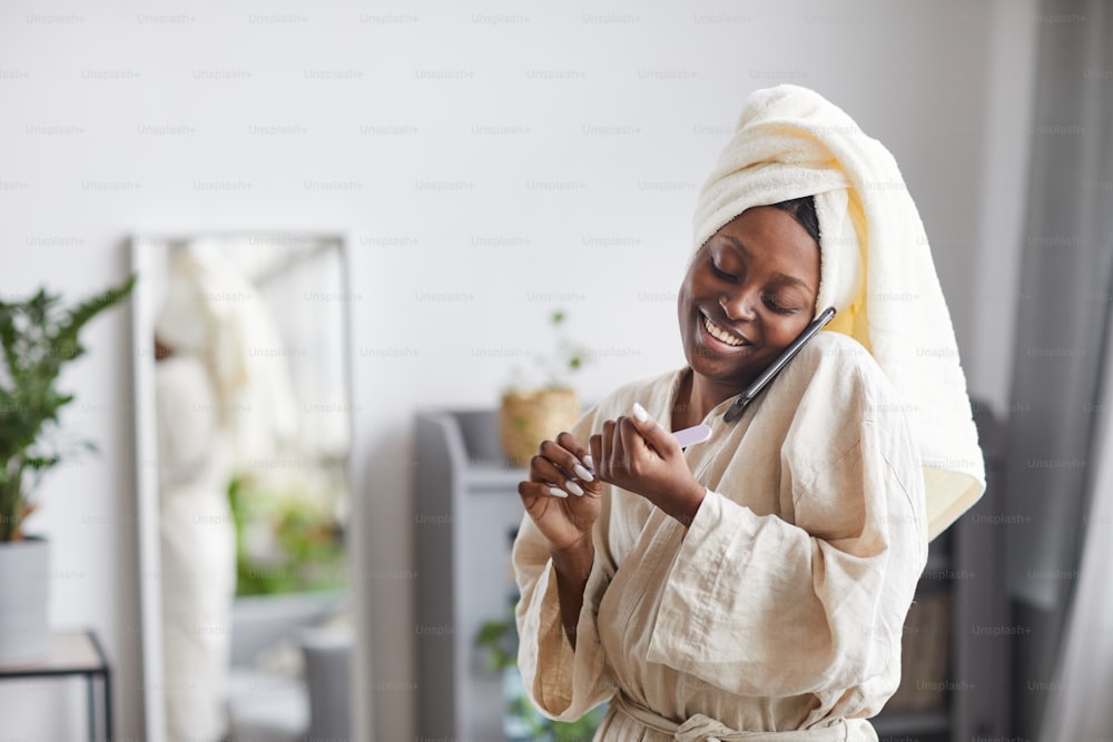 Portrait of young African-American woman enjoying beauty routine at home and speaking by smartphone, copy space