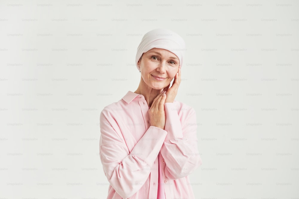 Retrato minimalista de una elegante mujer madura con pañuelo en la cabeza y mirando a la cámara mientras está de pie contra el blanco celebrando la recuperación del cáncer de mama, copia el espacio