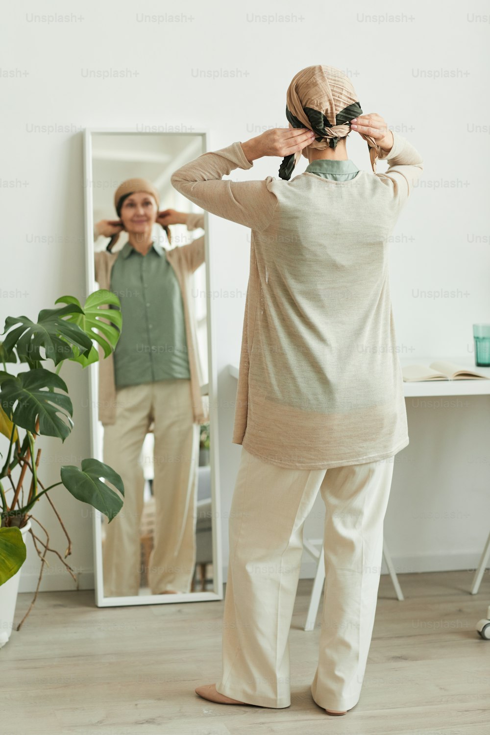 Rückenansicht in voller Länge bei reifer Frau, die am Spiegel ein Kopftuch aufsetzt und sich auf das Ausgehen vorbereitet