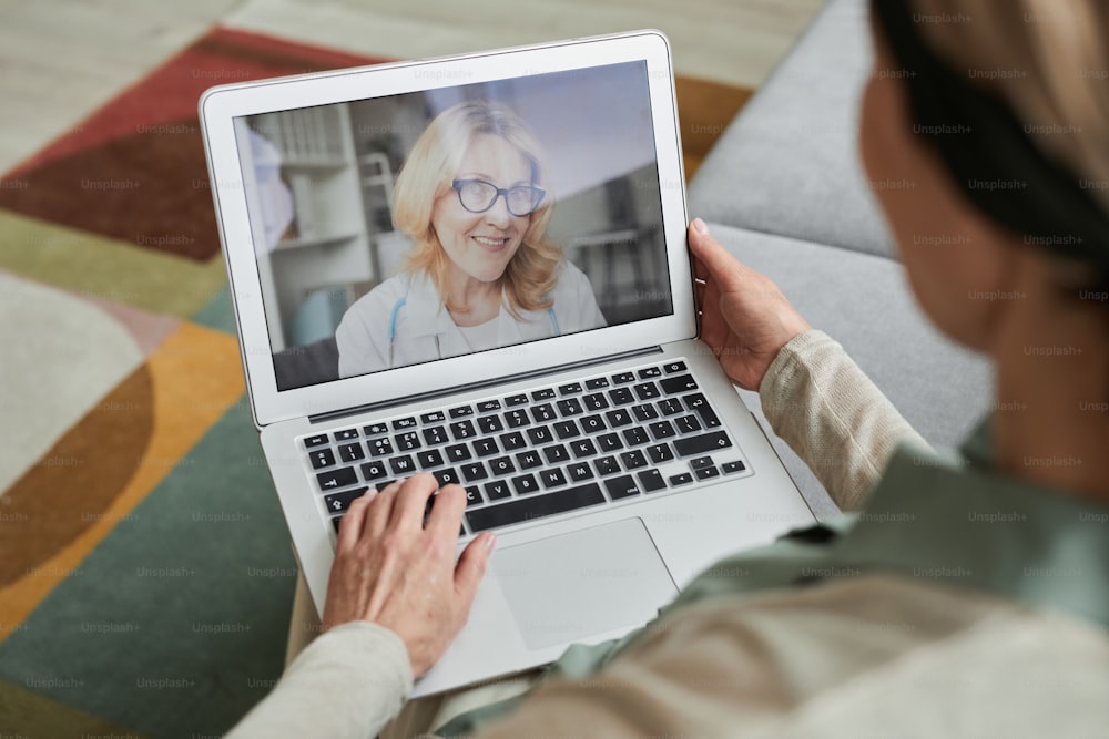 Visão de alto ângulo na mulher madura conversando com o médico do sexo feminino na tela do laptop por bate-papo por vídeo, espaço de cópia