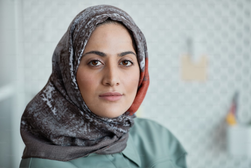 Retrato de perto da mulher confiante do Oriente Médio usando lenço de cabeça no escritório e olhando para a câmera, espa�ço de cópia