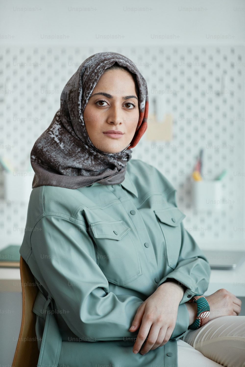 Vertikales Porträt einer selbstbewussten Frau aus dem Nahen Osten, die im Büro Kopftuch trägt und in die Kamera schaut