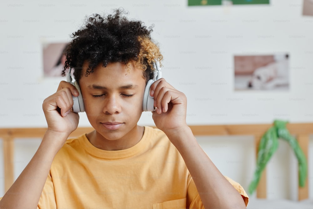 Retrato de un adolescente mestizo con auriculares y escuchando música con los ojos cerrados, copia el espacio
