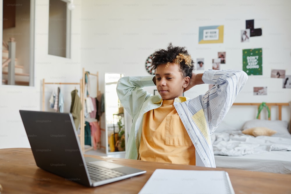 Retrato de un adolescente de raza mixta relajándose en casa y usando una computadora portátil en el acogedor interior de la habitación, espacio de copia
