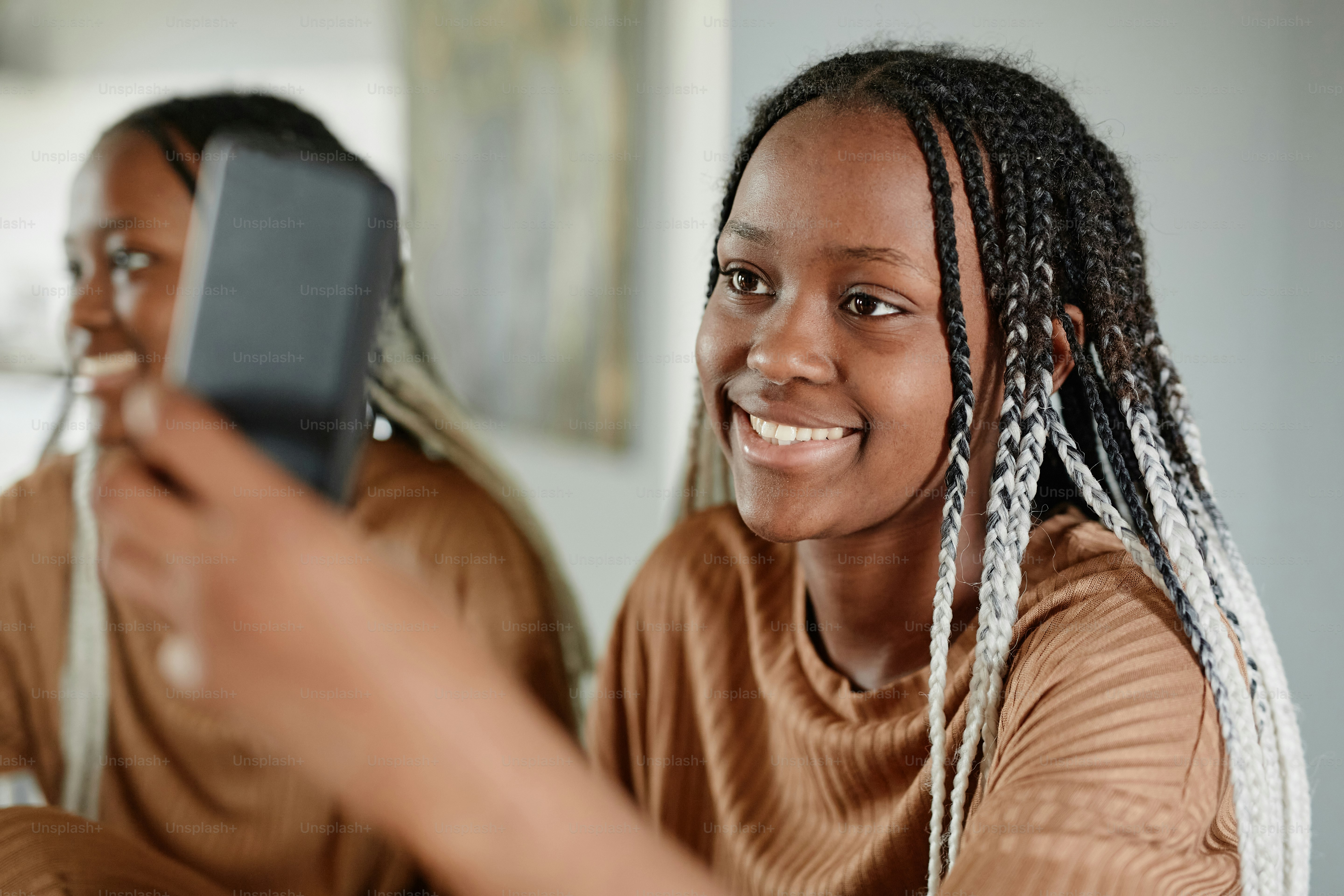 Portrait of young African-American woman video chatting with friends via smartphone and smiling