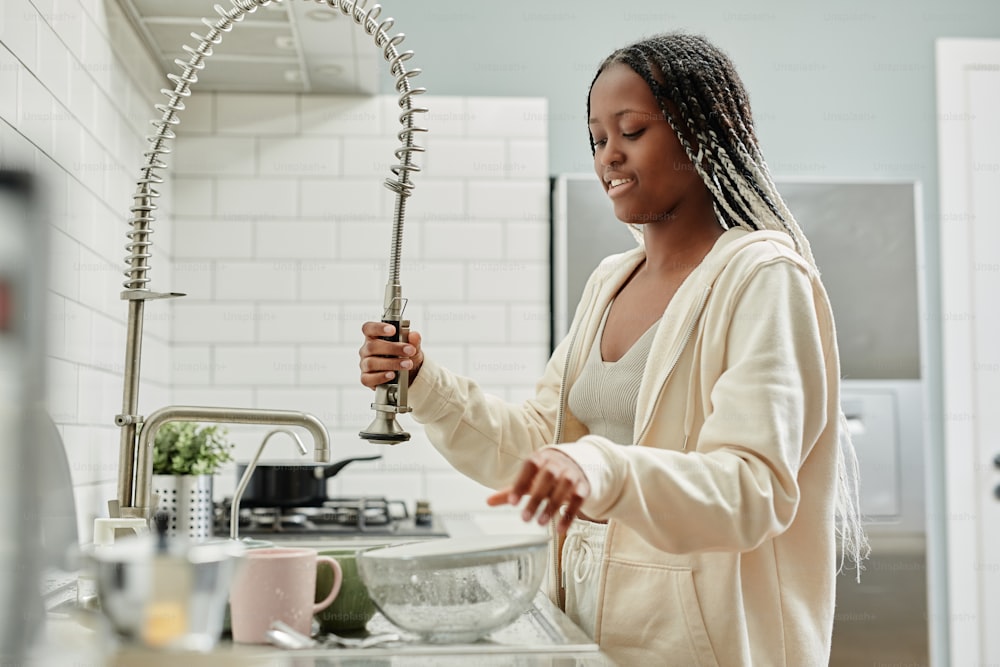 Portrait of young African-American woman washing dishes at home while doing chores on weekend, copy space