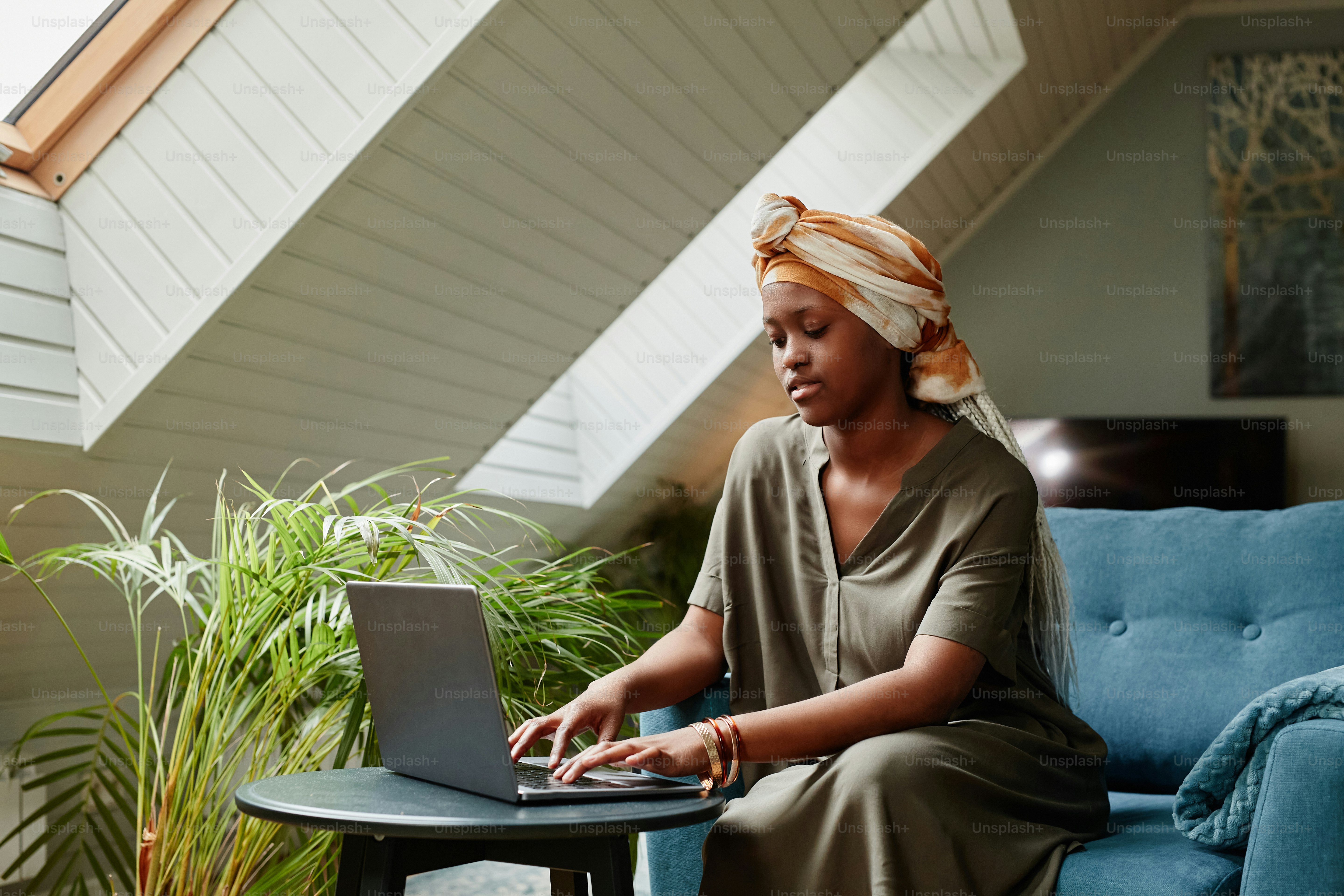Portrait of young African-American woman using laptop at home while working freelance, copy space