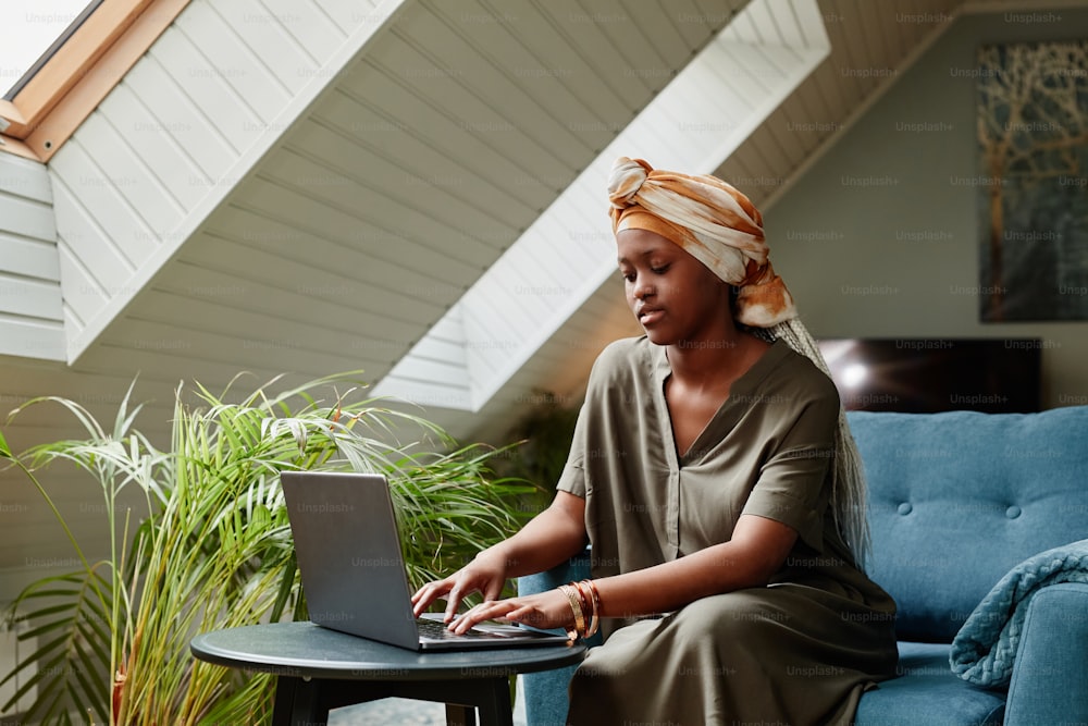 Portrait of young African-American woman using laptop at home while working freelance, copy space