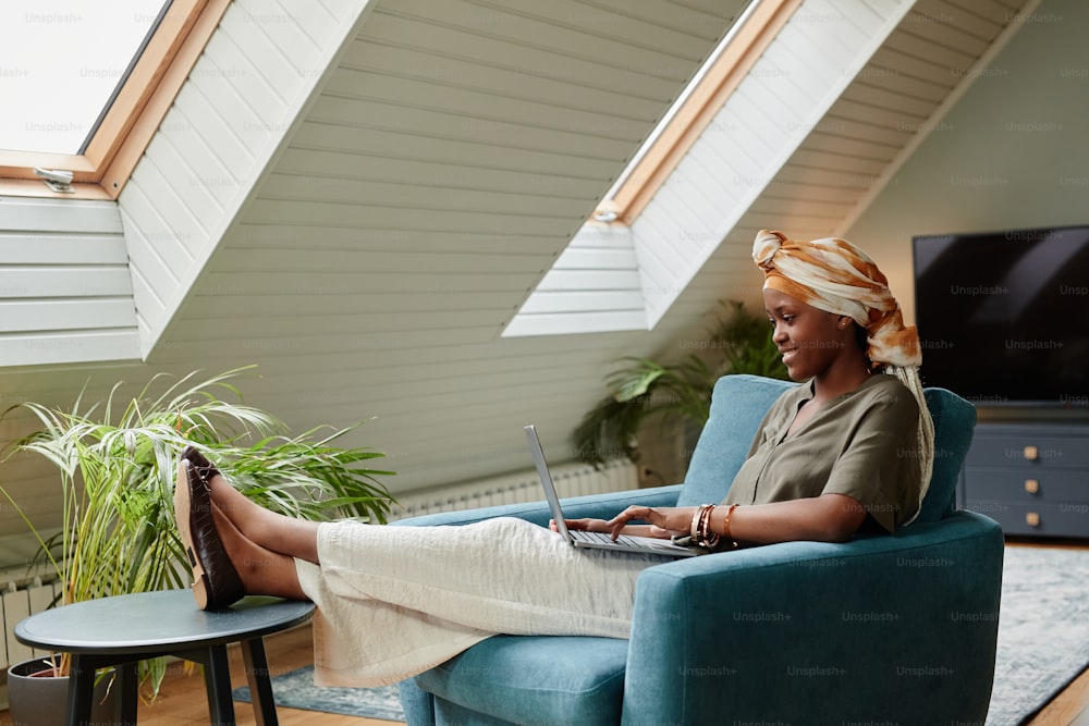 Side view portrait of young African-American woman relaxing at home and using laptop, copy space