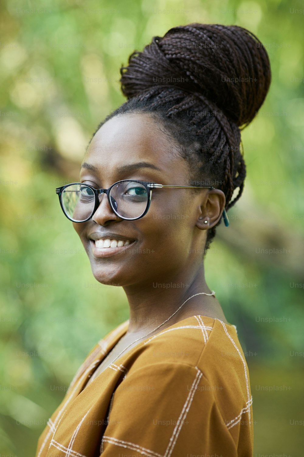 Vertical portrait of young African-American woman wearing glasses and smiling at camera outdoors in park