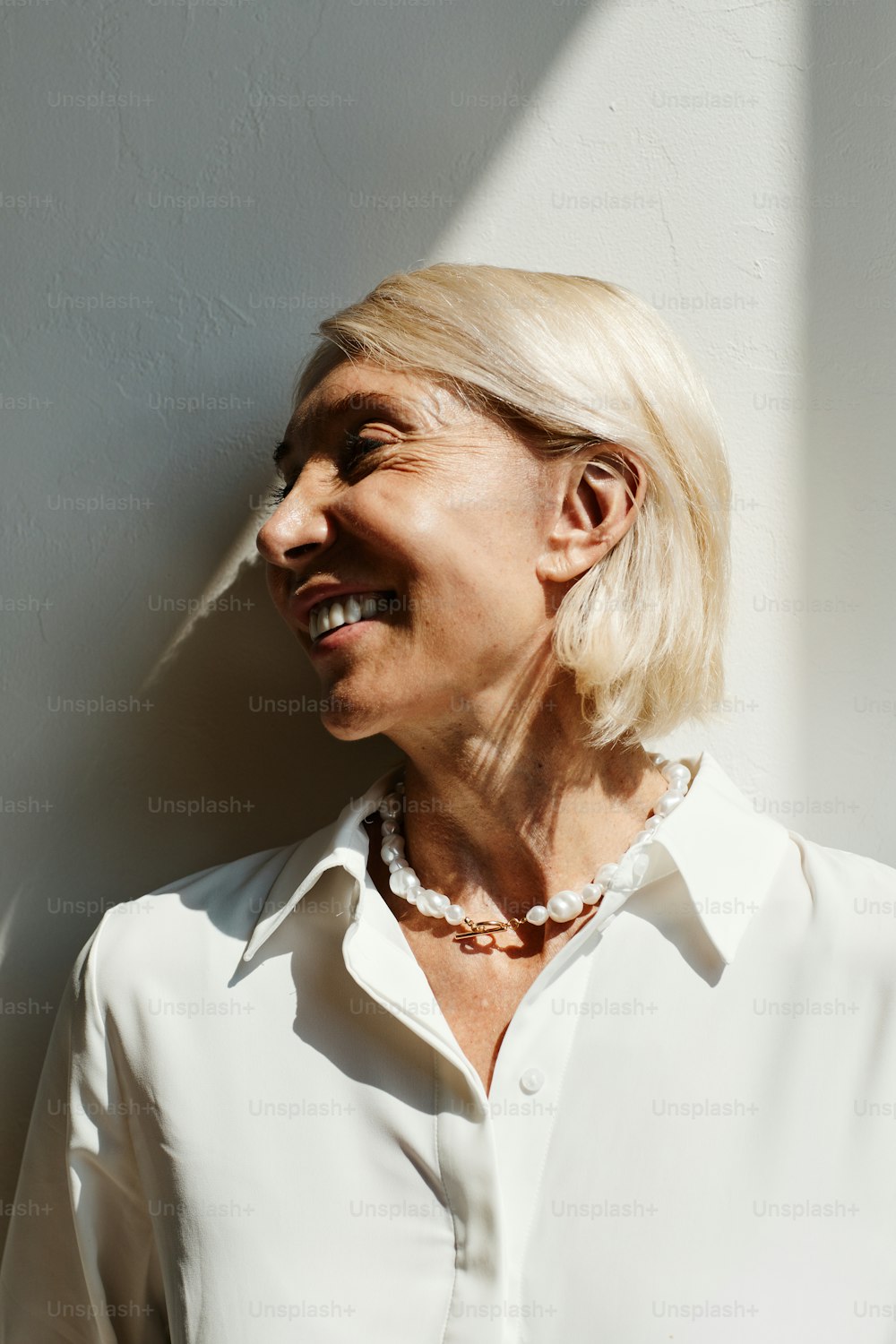 Minimal side view portrait of elegant mature woman lit by sunlight against white wall