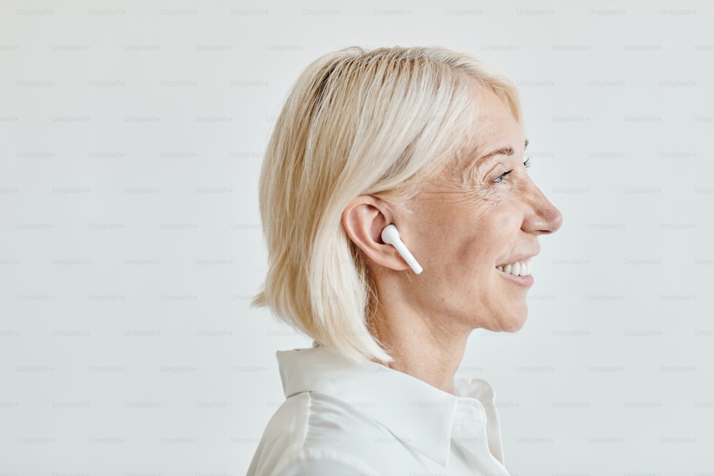 Vue latérale portrait d’une femme mûre élégante avec des écouteurs sans fil au point, espace de copie