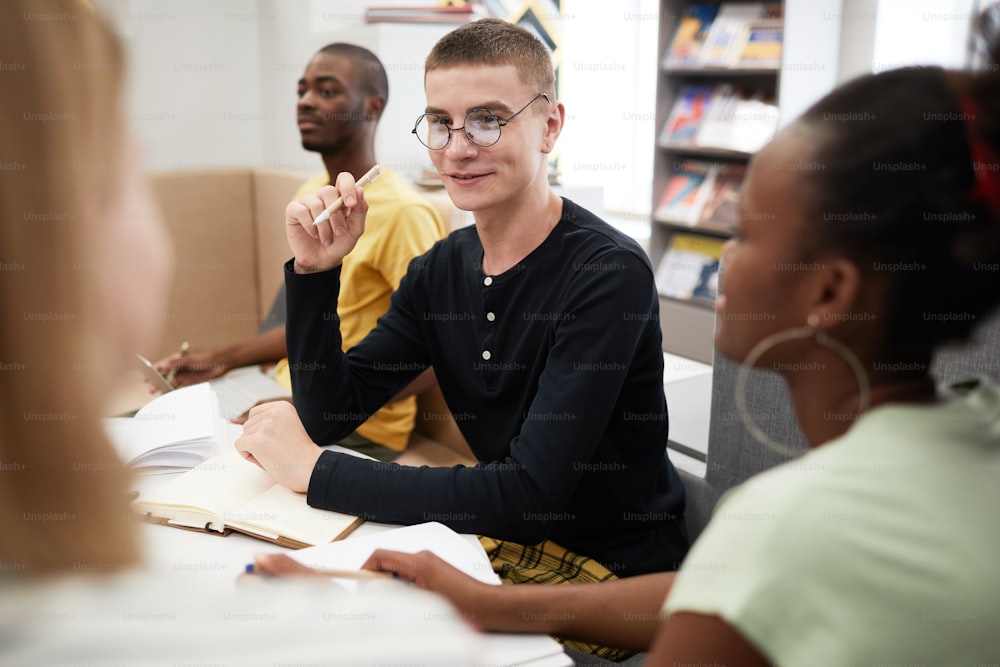 Portrait of smiling young man studying with group of friends in college library