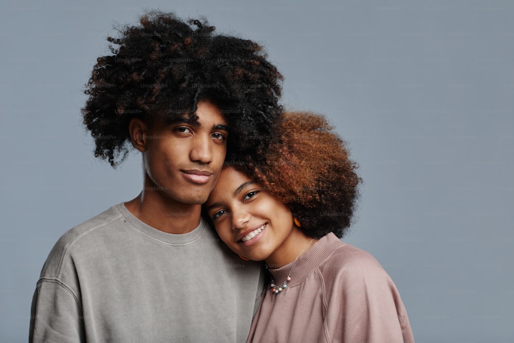 Portrait minimal d’un jeune couple afro-américain aux cheveux bouclés naturels souriant à la caméra sur fond bleu, espace de copie