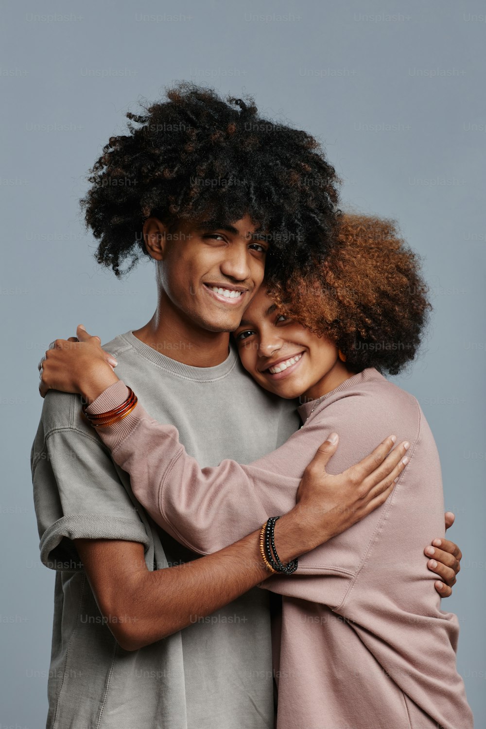 Portrait vertical minimal d’un jeune couple afro-américain aux cheveux bouclés naturels souriant à la caméra sur fond bleu, espace de copie