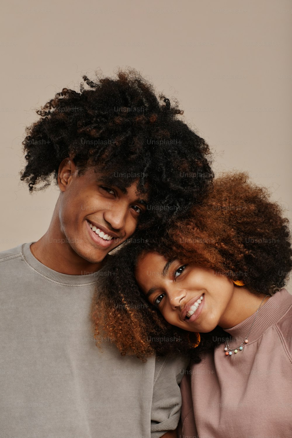 Minimal portrait of young African-American couple with natural curly hair smiling at camera while standing against light beige background