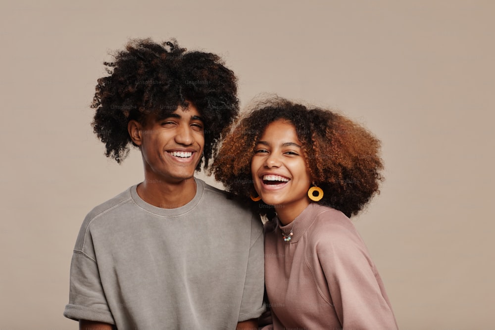 Portrait minimal d’un jeune couple afro-américain aux cheveux bouclés naturels souriant à la caméra sur fond beige, espace de copie