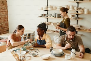 Retrato en tonos cálidos de un grupo diverso de personas disfrutando del taller de cerámica en un acogedor estudio