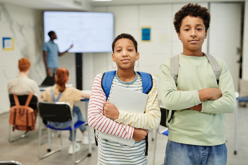 Cintura para cima retrato de dois adolescentes olhando para a câmera na sala de aula da escola, espaço de cópia