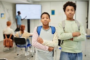 Waist up portrait of two teenage kids looking at camera in school classroom, copy space
