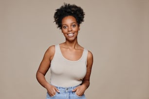 Minimal waist up portrait of young African-American woman smiling at camera while standing against neutral background, natural beauty