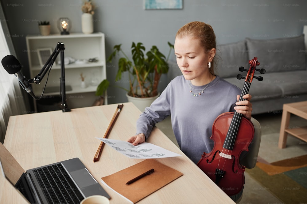 Hochwinkelporträt einer blonden Frau, die zu Hause Geige spielt und beim Komponieren Notenblätter betrachtet, Kopierraum