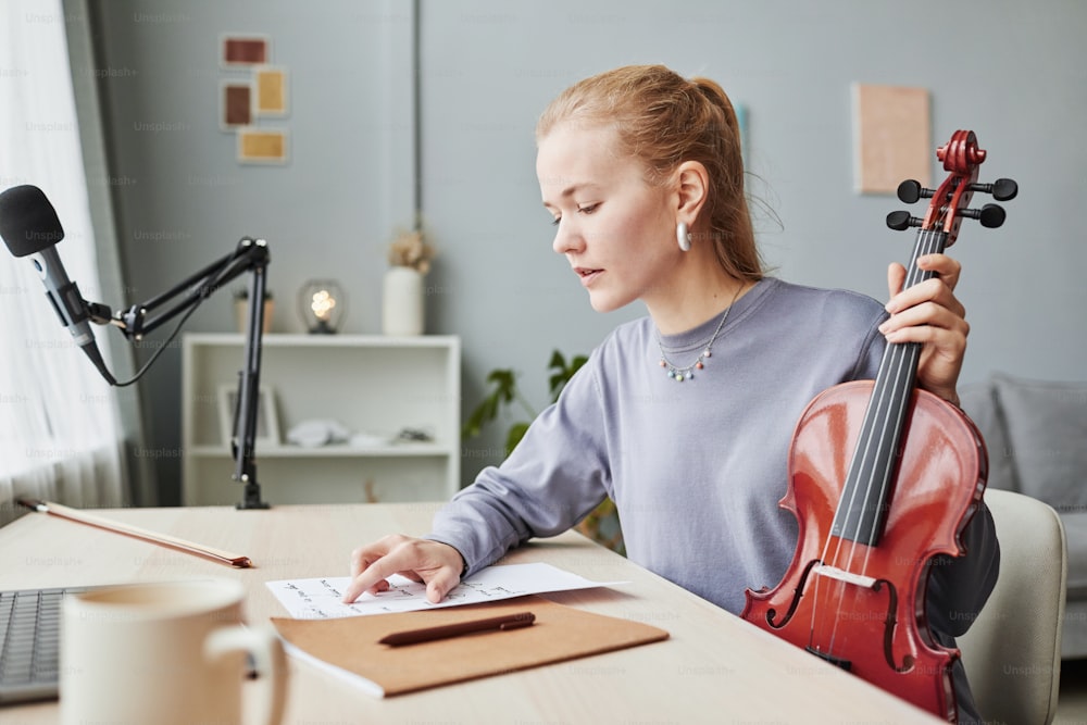 Seitenansicht Porträt einer blonden Frau, die zu Hause Geige spielt und beim Komponieren Notenblätter betrachtet, Kopierraum