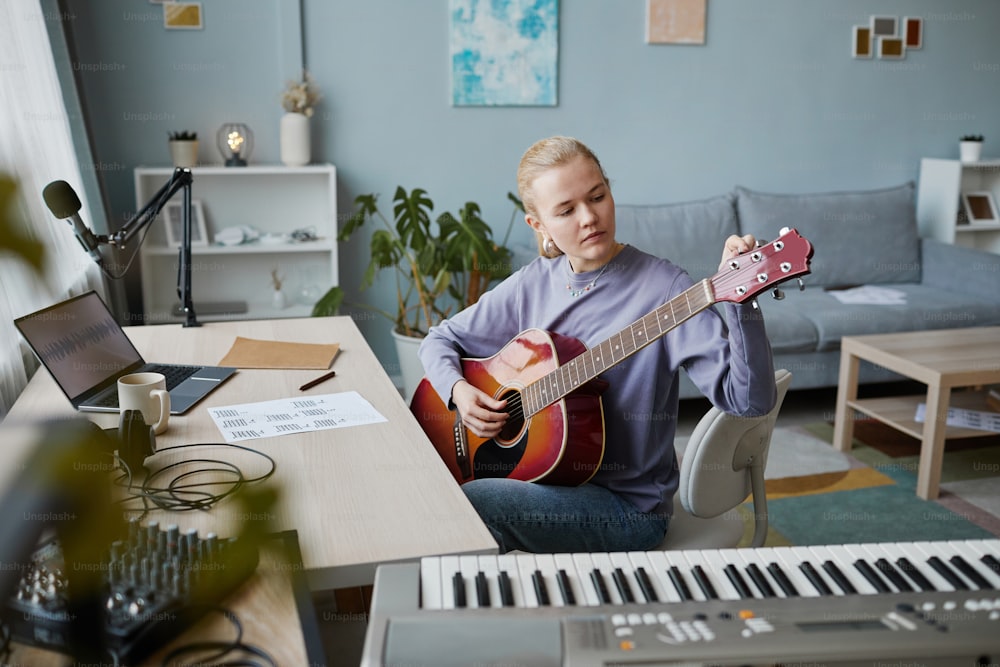 Retrato da mulher jovem loira que joga guitarra em casa e compõe a faixa de música usando o software de gravação