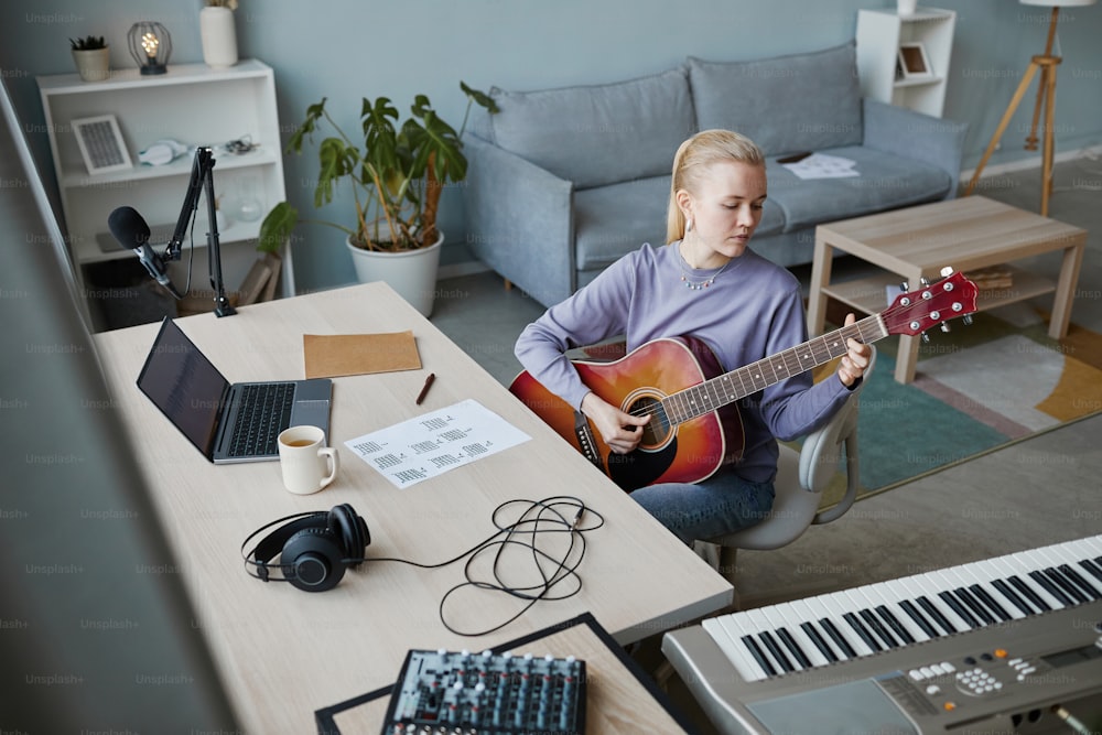 Hochwinkelporträt einer blonden jungen Frau, die zu Hause Gitarre spielt und Musik komponiert, Kopierraum
