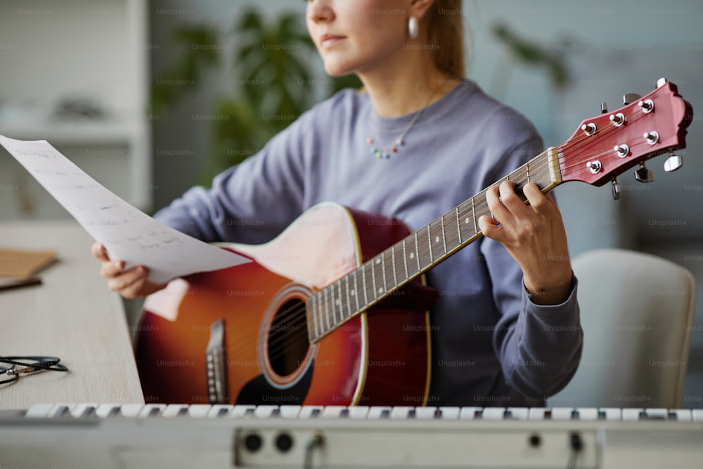 Close up da jovem mulher segurando a partitura de música enquanto toca guitarra em casa ou no estúdio, espaço de cópia