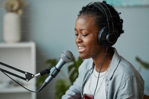 Ritratto di vista laterale minimale della giovane donna nera che canta al microfono nello studio di registrazione di casa, spazio di copia