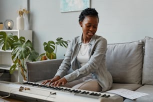 Portrait d’une jeune femme noire jouant du synthétiseur à la maison et composant de la musique dans un cadre confortable à la maison, espace de copie