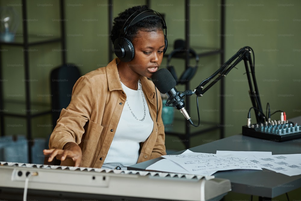 Portrait d’une jeune femme noire chantant au micro tout en enregistrant de la musique à la maison