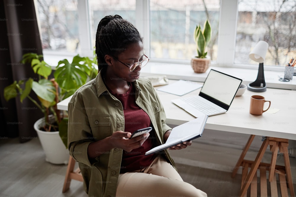 현대 아프리카계 미국인 여성의 초상화는 재택근무를 하고 최소한의 실내에서 노트북을 사용하며 공간을 복사합니다