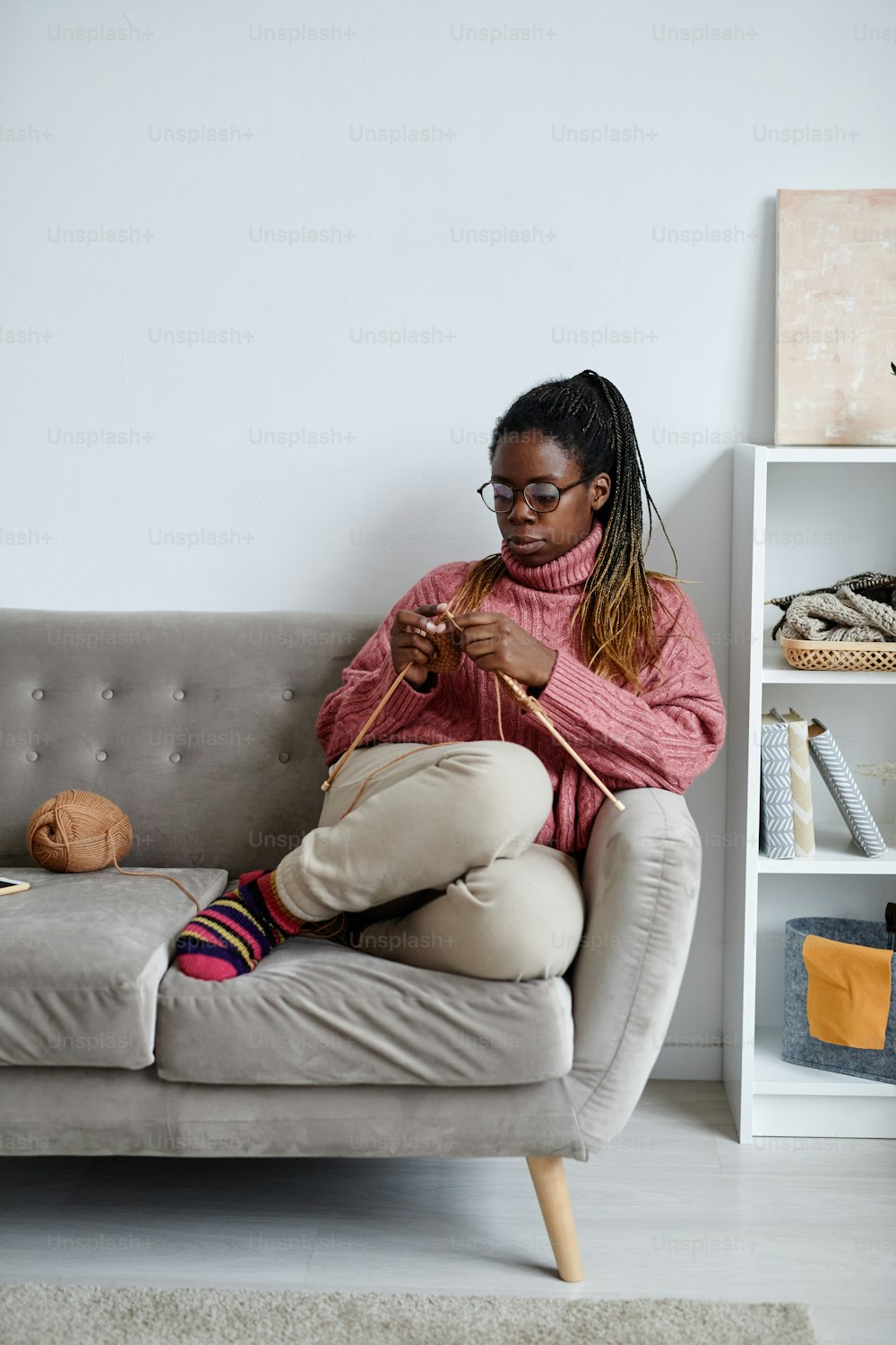 Vertical full length portrait of young African-American woman knitting while enjoying cozy weekend at home
