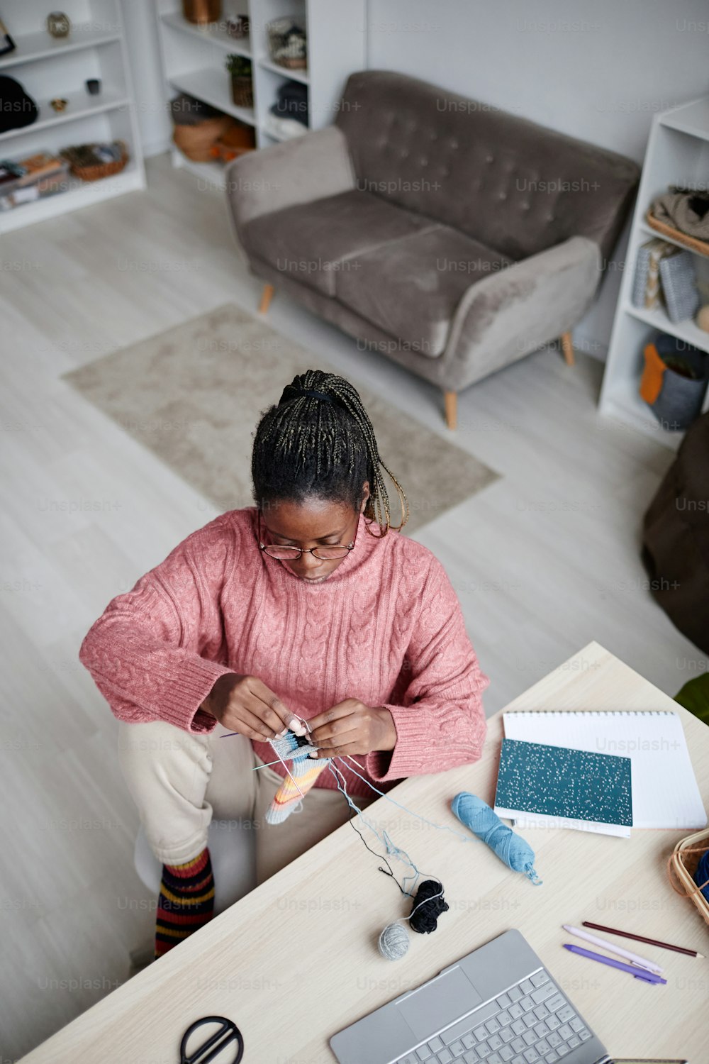 Ritratto ad angolo alto della giovane donna afroamericana che lavora a maglia a casa in una stanza accogliente, spazio di copia