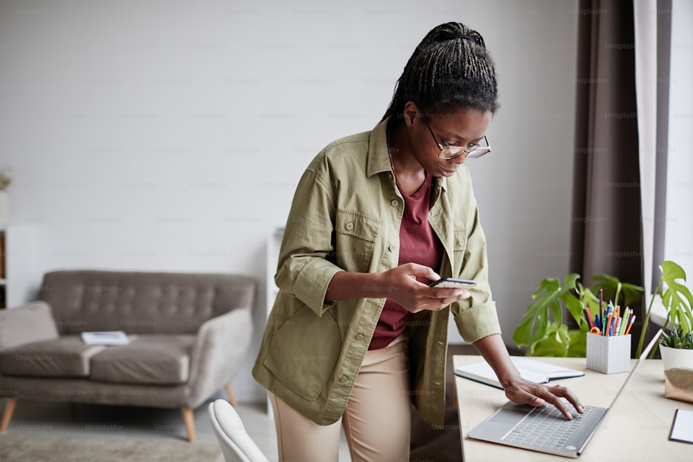 Portrait d’une femme afro-américaine contemporaine travaillant à domicile et utilisant un ordinateur portable dans un intérieur minimal, espace de copie
