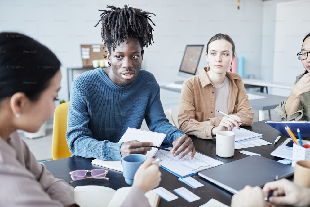 Portrait of young black man in group discussion at English seminar in office, copy space